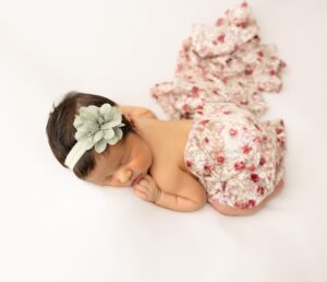 Baby girl wearing a green headband and wrapped in a floral lace for a newborn photoshoot.