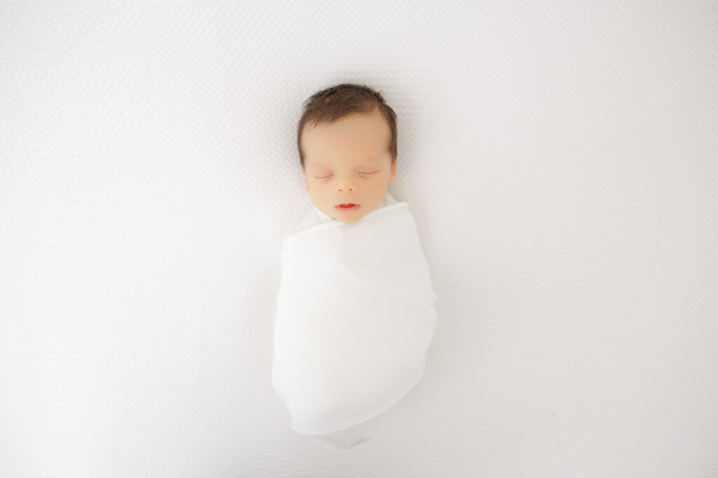 Newborn wrapped in a snugly white blanket and posed at Heather Nicole Photography.