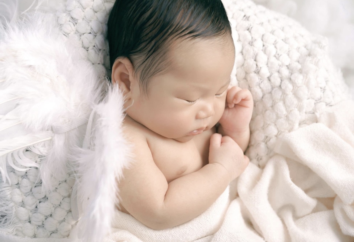 Baby Boy sleeping soundly with angel wings on back and wrapped in a sift off-white blanket.