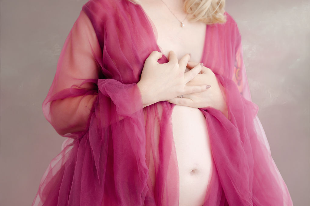 Details of a pregnant woman's bump peeking out of a pink tule maternity gown