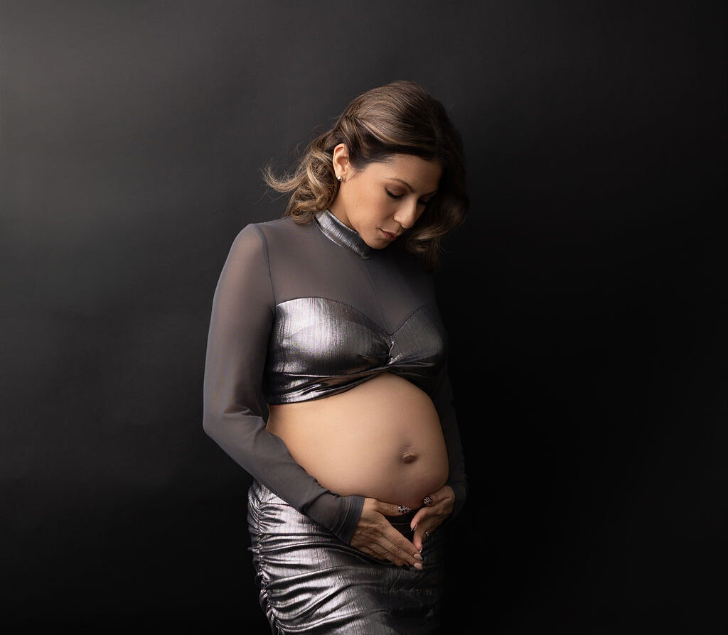 A mother to be stands in a silver designer outfit gazing down to the bump with hands under it after a 3d ultrasound in redondo beach
