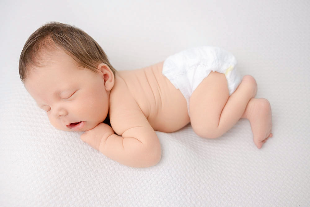 A sleeping newborn baby in a diaper on a white blanket