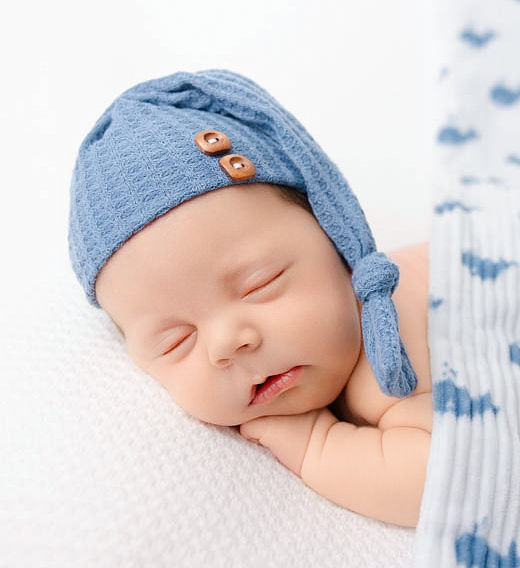 A newborn baby sleeps in a blue nightcap under a white and blue blanket after meeting with South Bay Nannies
