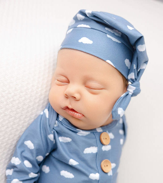 A sleeping newborn baby in cloud onesie and matching sleep cap thanks to South Bay Nannies
