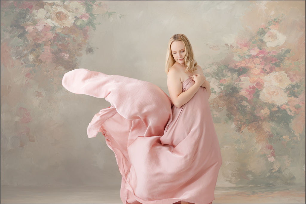 A mother to be stands in a studio wrapped in a flowing pink sheet as she looks back to it before visiting baby shower venues in redondo beach
