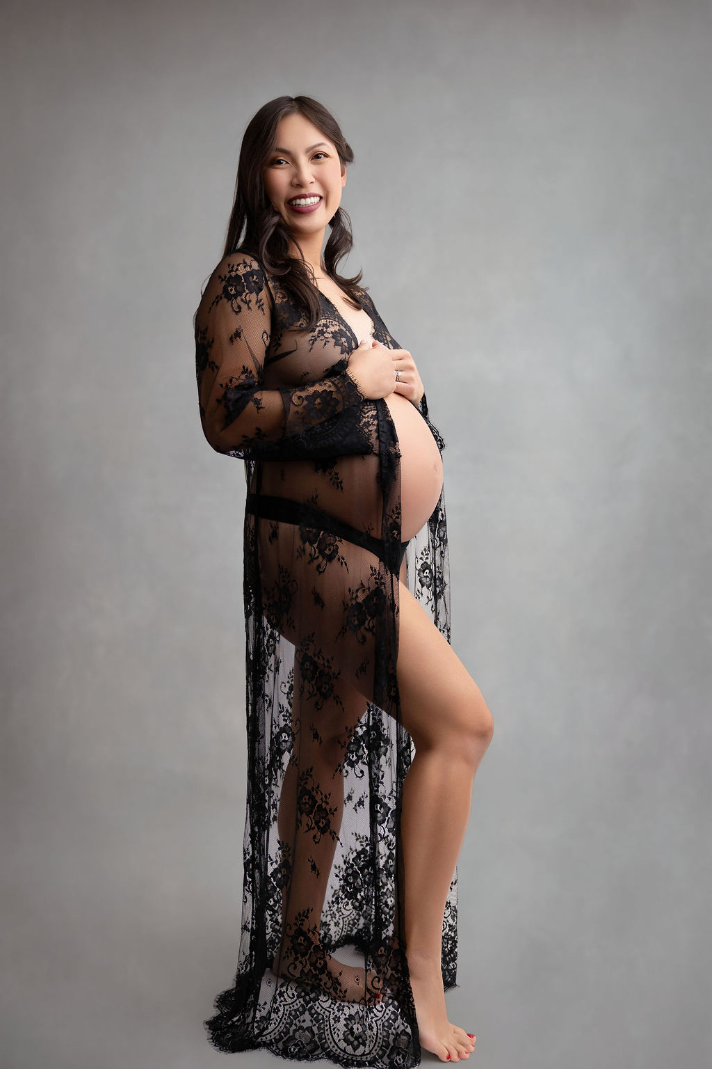 A smiling mother to be stands in a black lace robe in a studio after finding an obgyn in redondo beach