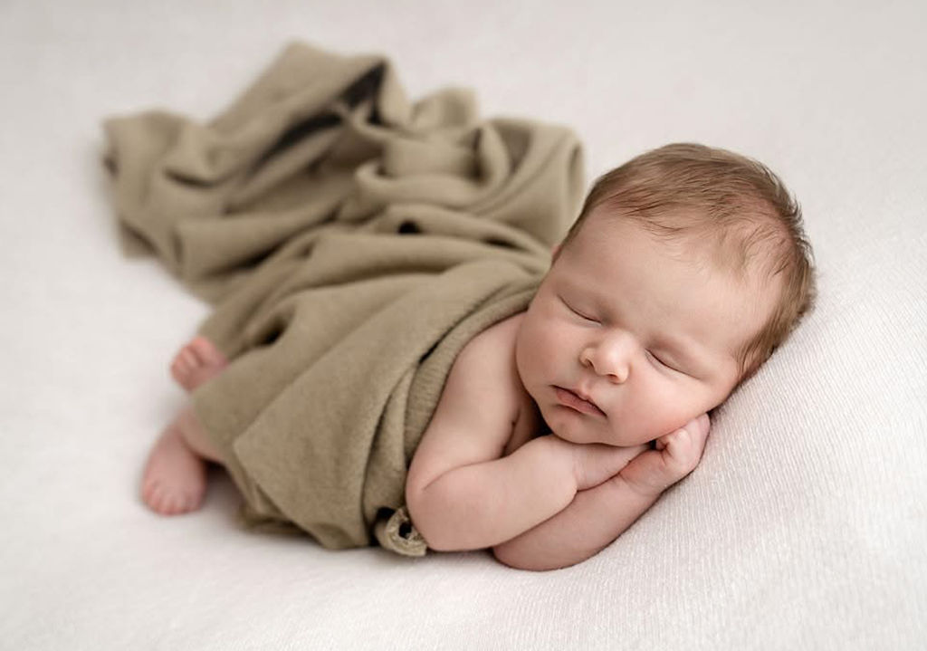 A sleeping newborn under a green blanket on his side after visiting pediatricians in redondo beach