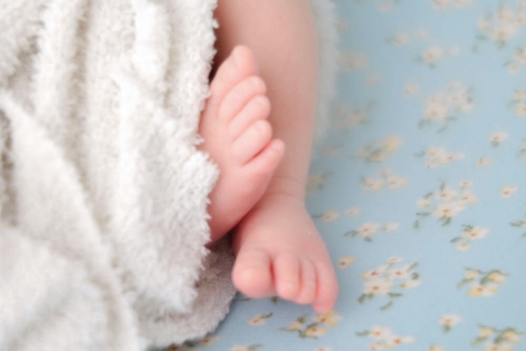 Details of a newborn baby's feet on a blue flower print bed