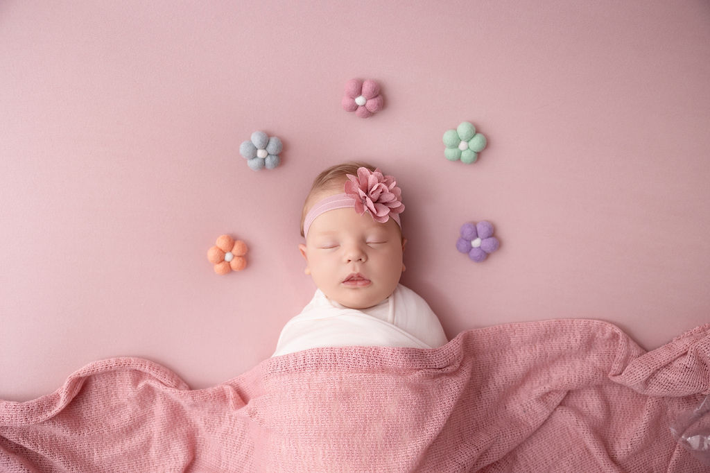 A sleeping newborn girl under a pink blanket with a flower headband thanks to postpartum doulas in redondo beach