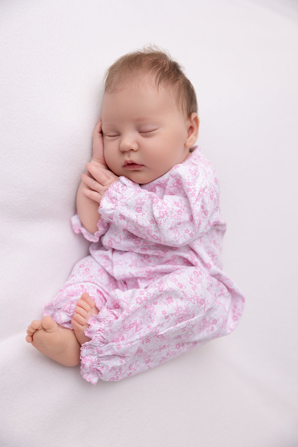 A newborn baby sleeps in pink pajamas with a hand under her head after meeting postpartum doulas in redondo beach