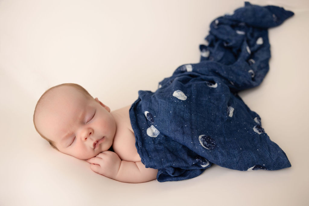A newborn baby sleeps under a blue moon pattern blanket in a studio