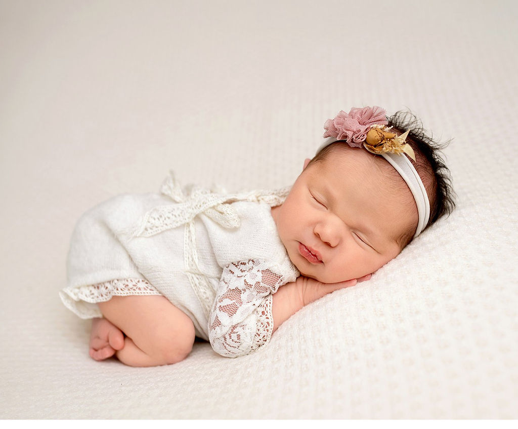 A sleeping newborn baby girl in a white lace onesie on a bed after some baby music classes in redondo beach