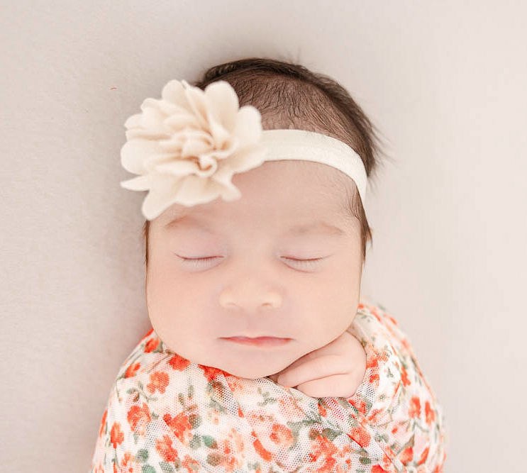 A closeup of a newborn baby sleeping in a pink floral swaddle and pink headband