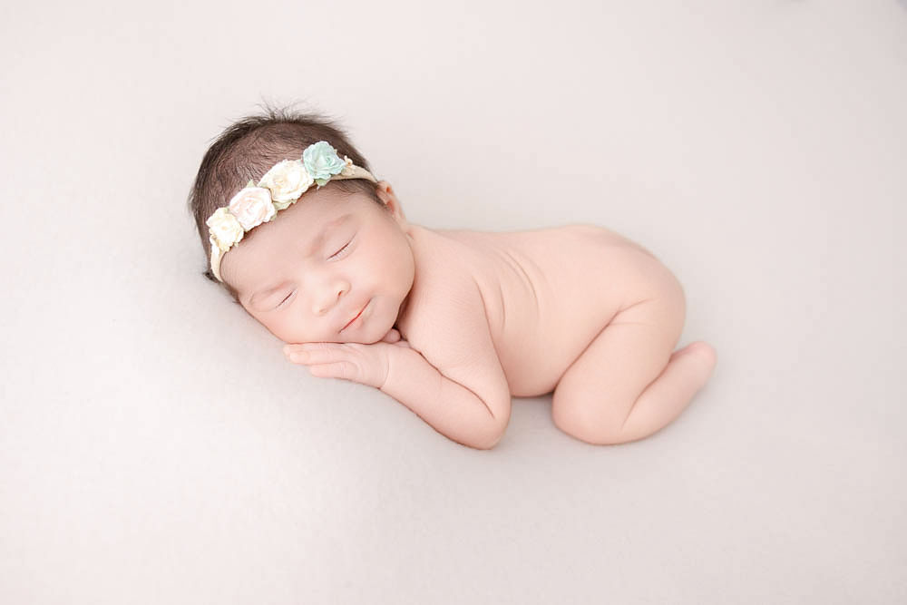 A newborn baby smiles in her sleeps with a flower headband after touring daycares in redondo beach