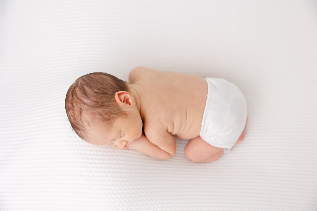 A sleeping newborn in a cloth diaper on a white bed after enjoying a diaper service in Southern California