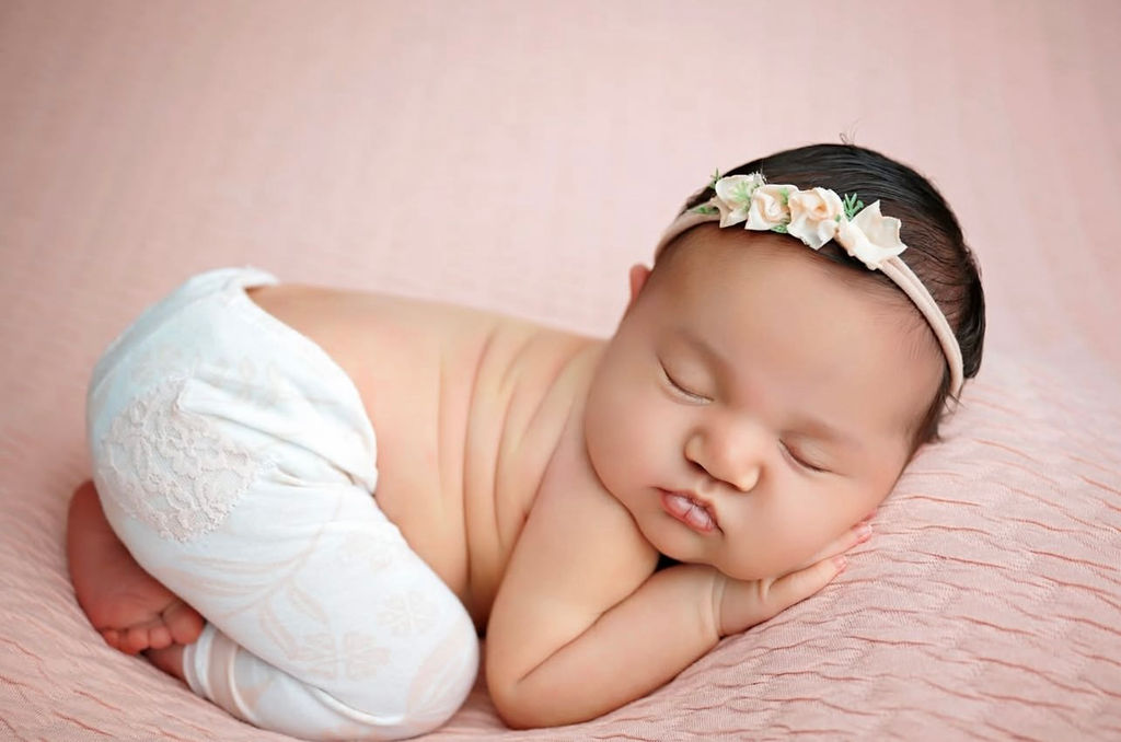 A newborn baby sleeps on her tummy in white pants on a pink bed after enjoying diaper service in Southern California