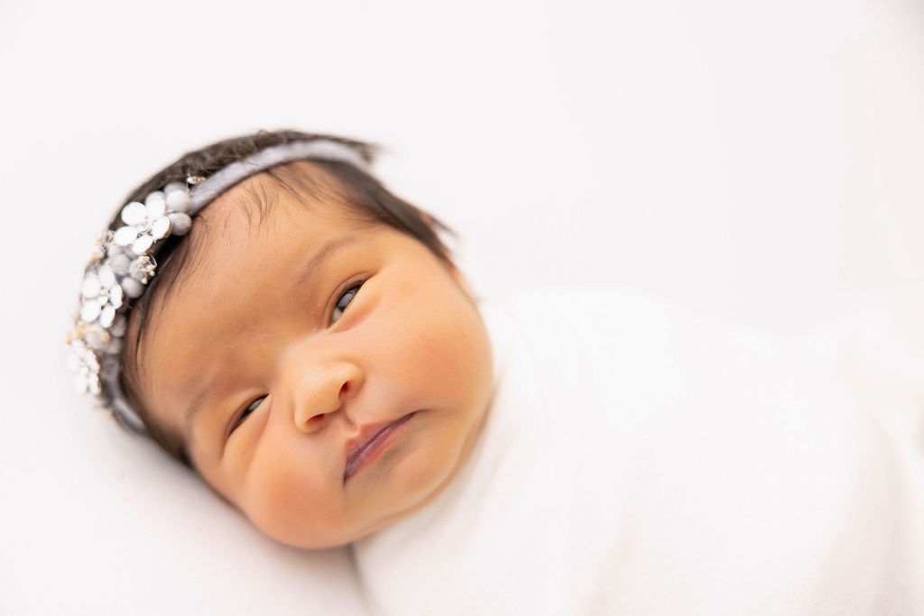 A closeup of a newborn baby looking around while in a white swaddle