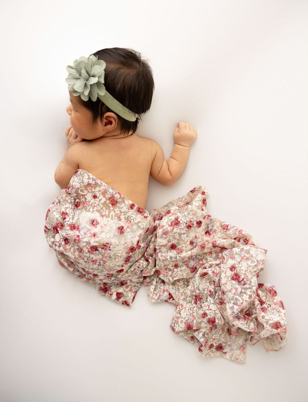 A look down at a newborn girl under a floral blanket on a white bed before some infant swim lessons in redondo beach