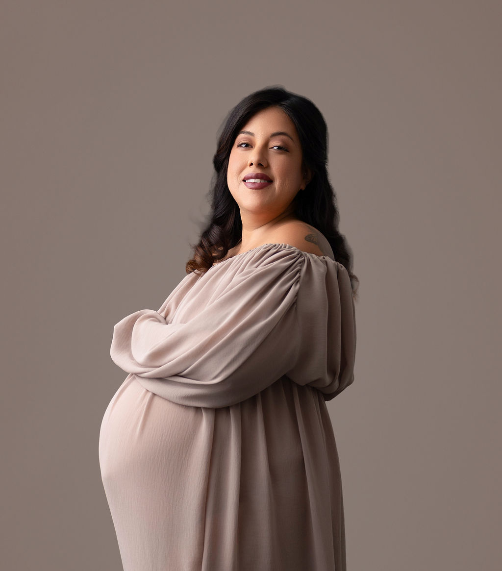 A mother to be in a flowing maternity gown stands smiling in a studio after a prenatal massage in redondo beach