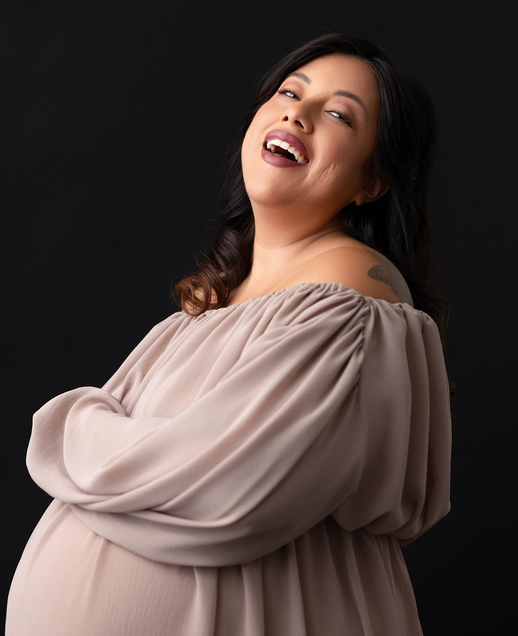 A happy pregnant woman laughs in a studio in a cream maternity dress after a prenatal massage in redondo beach
