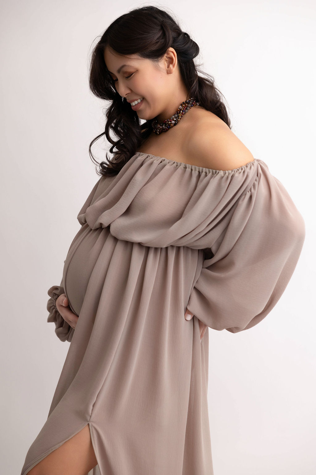 A happy pregnant woman laughs down at her bump with her hand under it