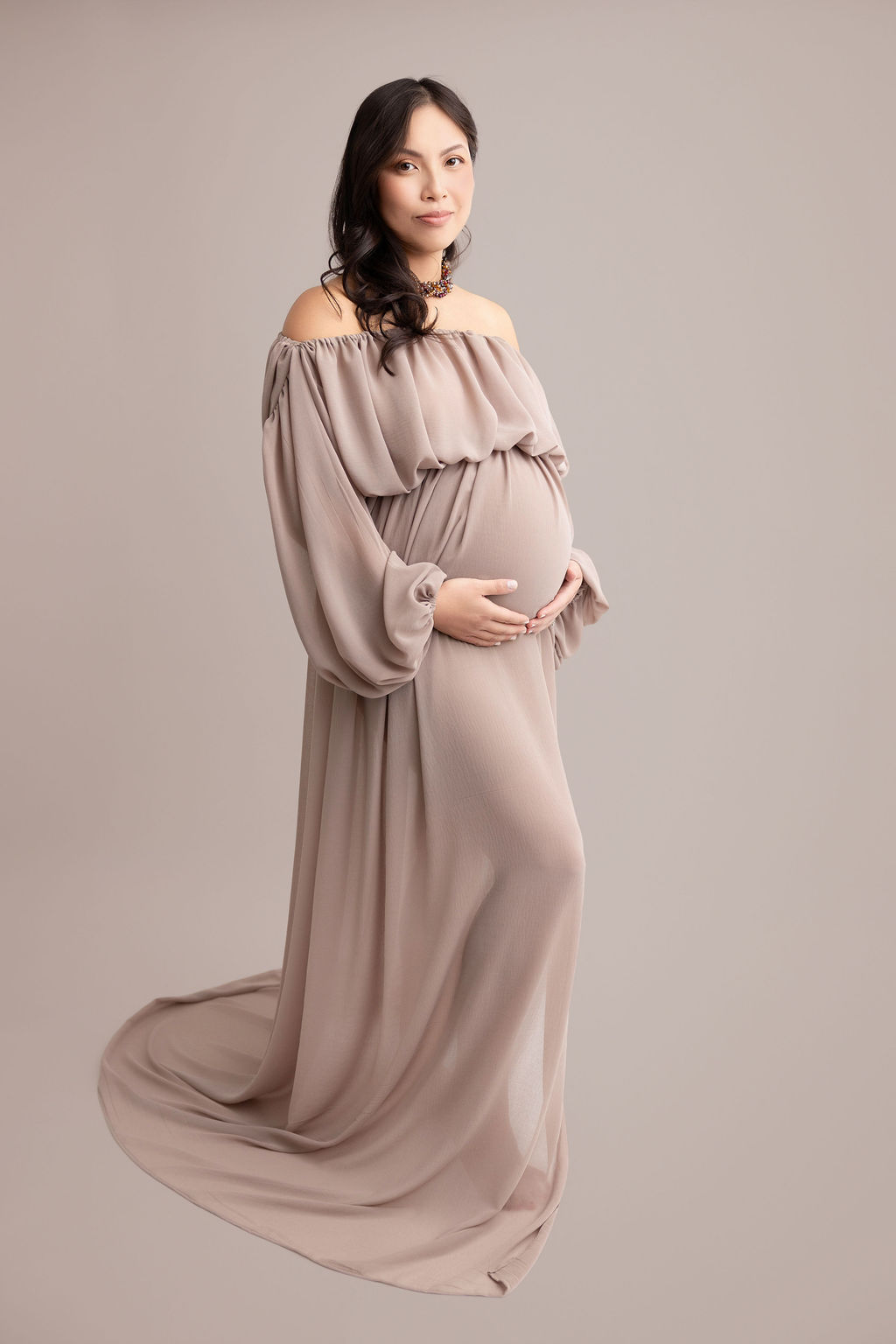 A smiling pregnant woman holds her bump in a loose flowing maternity gown in a studio after her 3d ultrasound in torrance