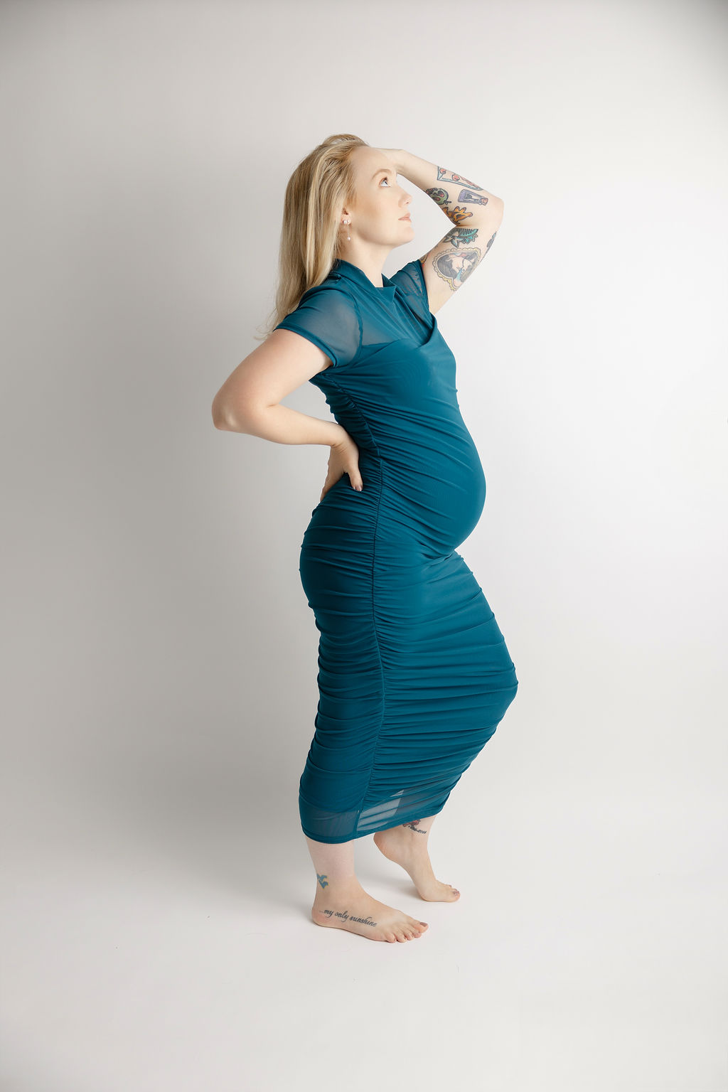 A mother to be stands in a teal maternity gown with a hand in her hair after visiting fertility clinics in torrance