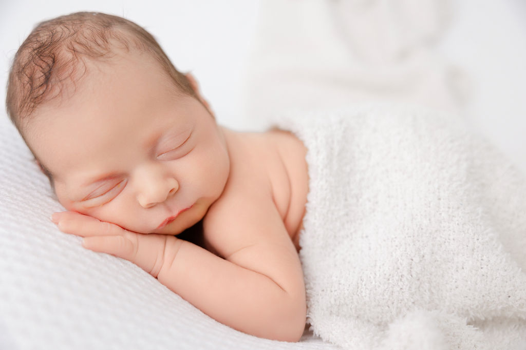 A newborn baby sleeps on a white bed under a blanket on its cheek thanks to lactation consultants in torrance