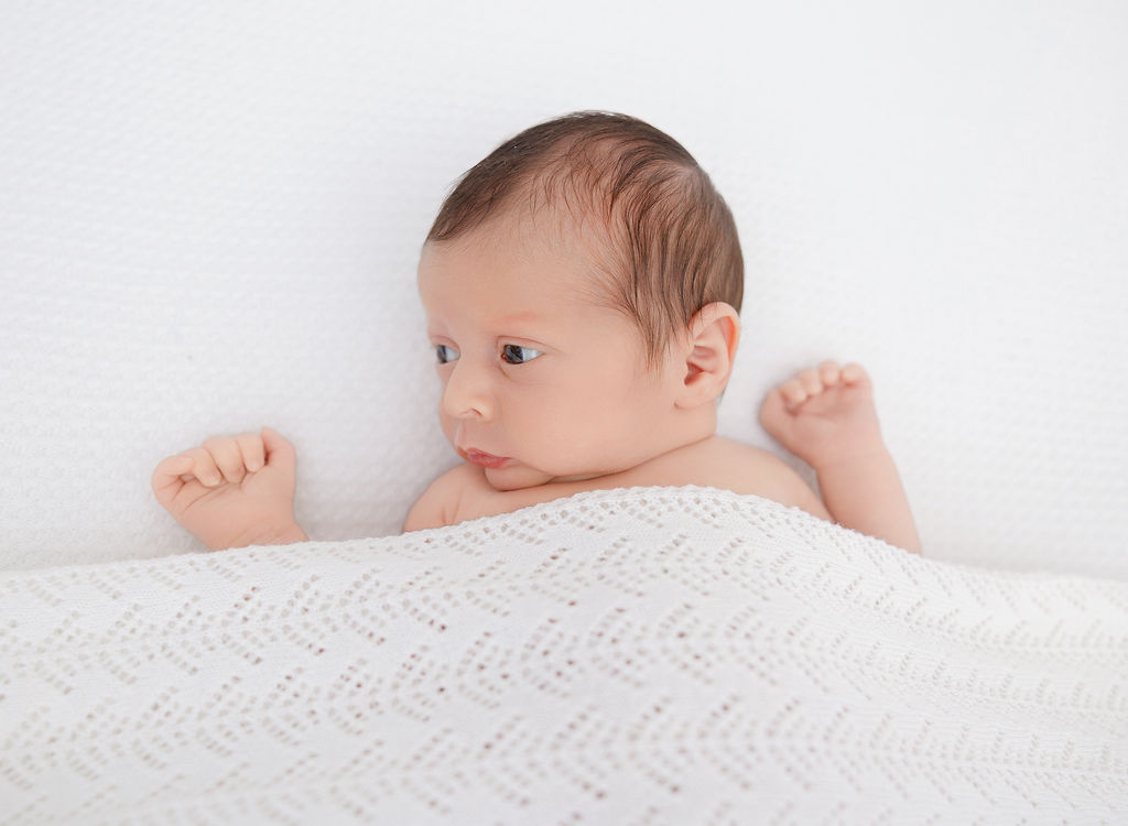 A newborn baby lays awake with eyes open under a white blanket after meeting lactation consultants in torrance