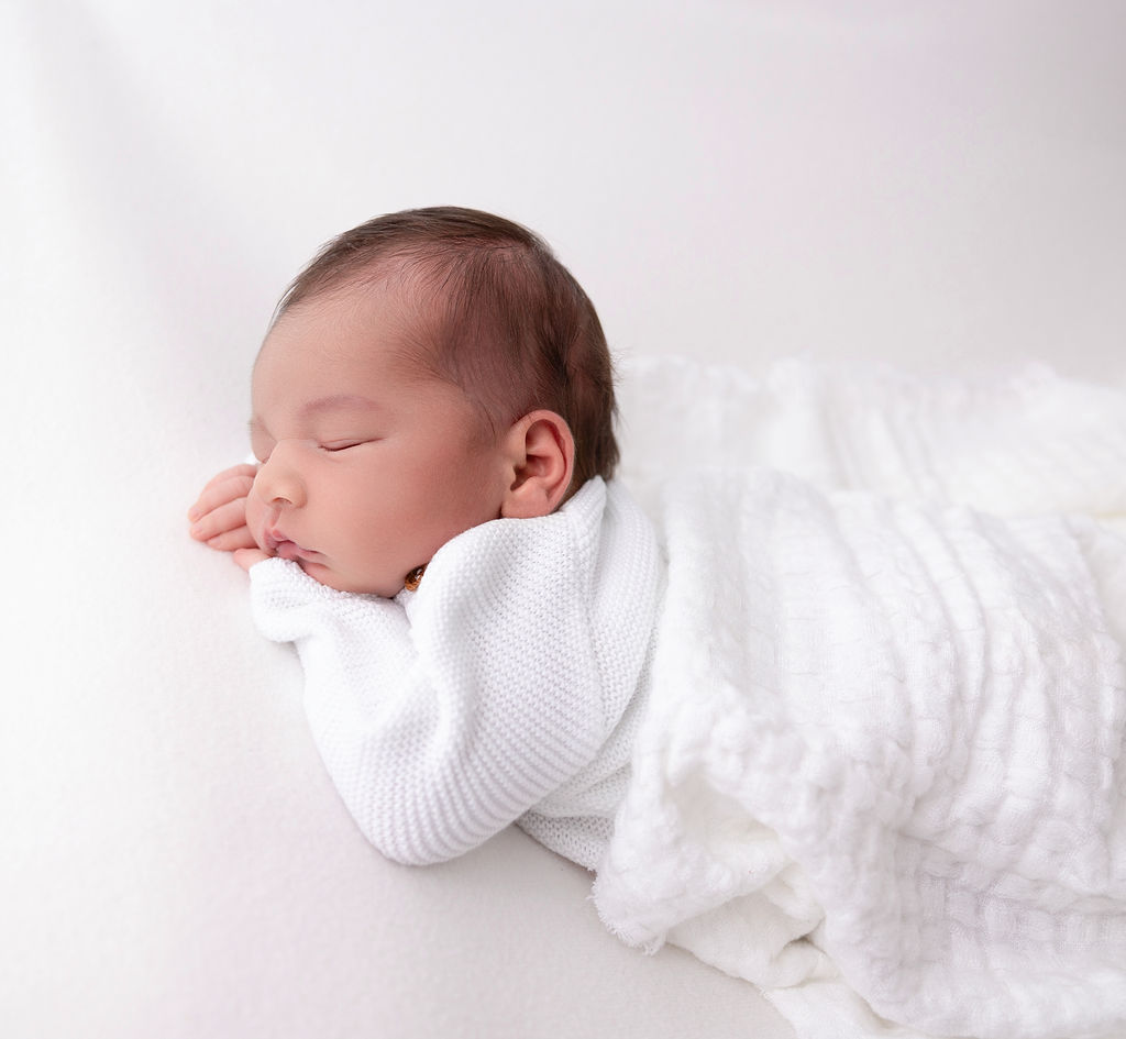 A sleeping newborn baby in a white sweater on its tummy after finding nannies in torrance