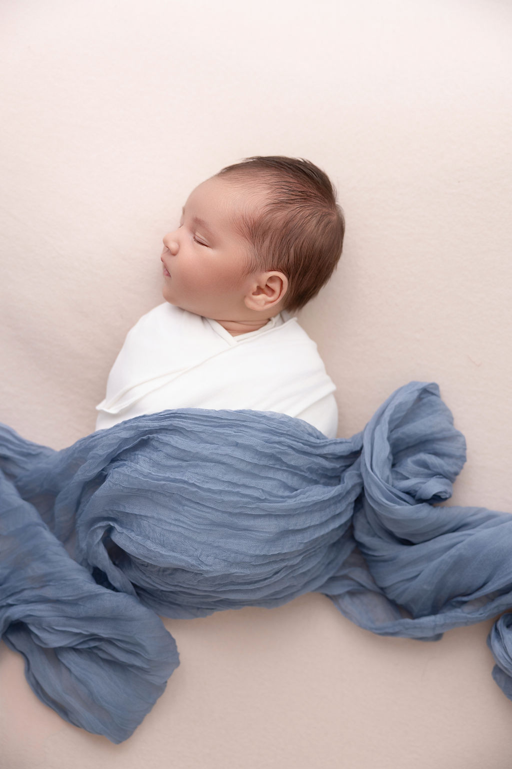 A newborn baby boy sleeps under a blue fabroc in a white swaddle after meeting nannies in torrance