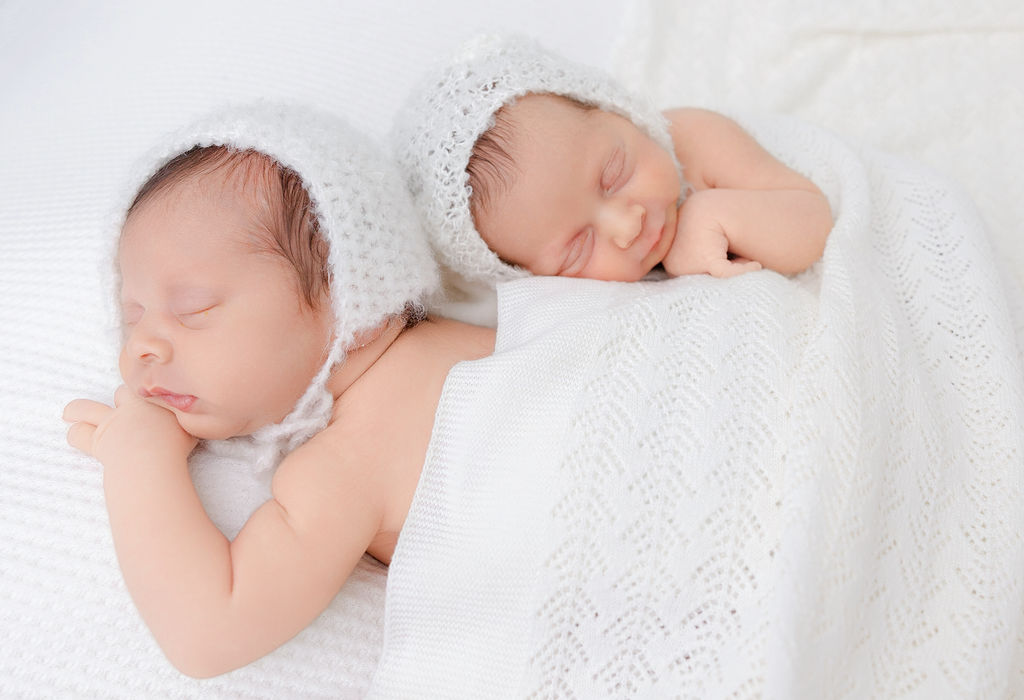 Newborn twins snuggle in white knit bonnets