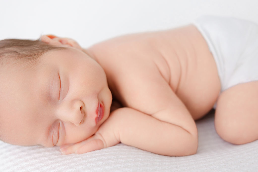 A sleeping newborn baby with pursed lips in a cloth diaper on his tummy after finding great pediatric dentists in torrance
