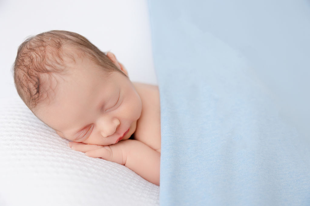 A newborn baby sleeps under a blue blanket on a white bed after visiting pediatric dentists in torrance