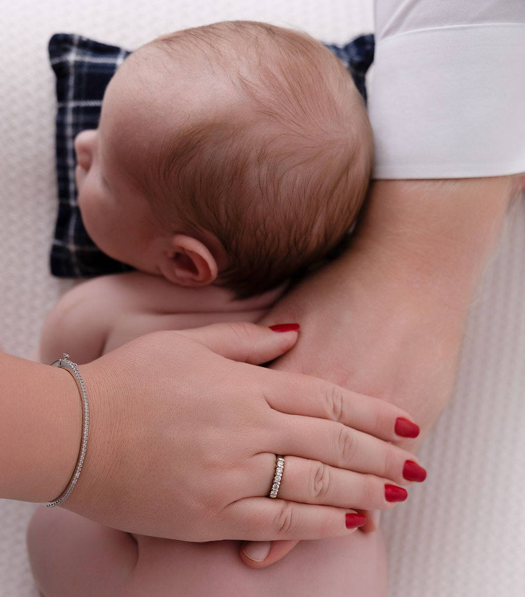 Details of mom and dad's hands resting on the back of their sleeping newborn baby on a whtie bed