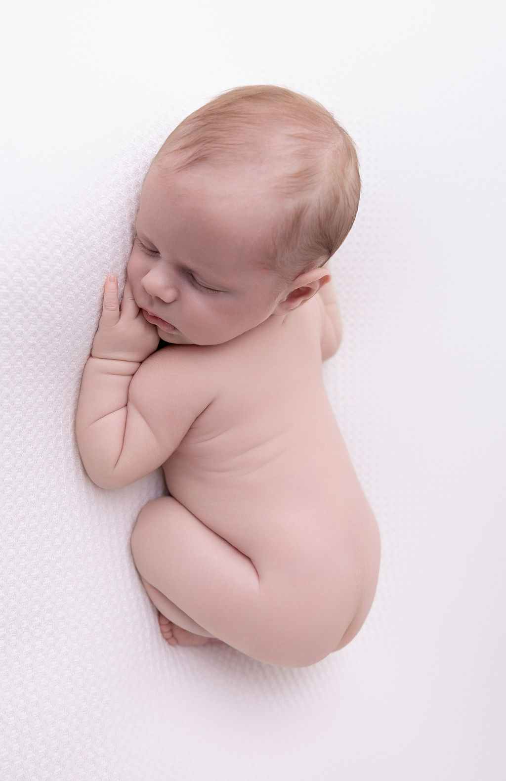 A naked newborn baby sleeps on a white bed in froggy pose after meeting pediatricians in torrance