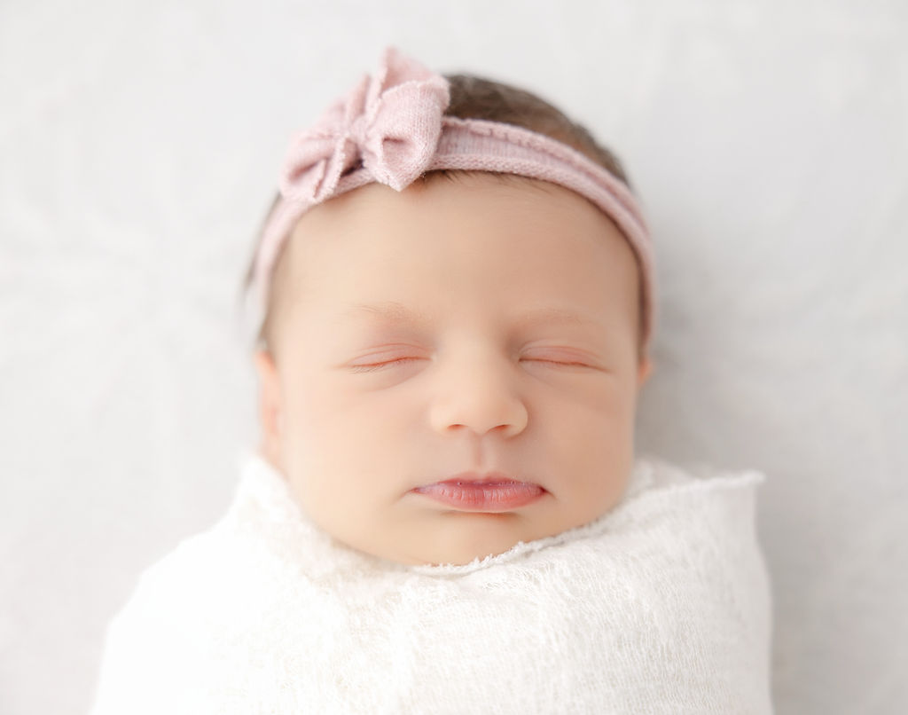 A closeup of a sleeping newborn baby girl with a pink headband bow after meeting postpartum doulas in torrance