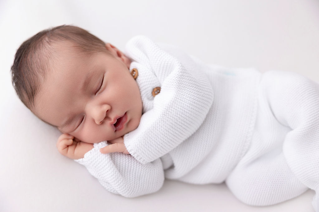 A sleeping newborn baby in a white knit onesie on its side thanks to parenting classes in torrance ca