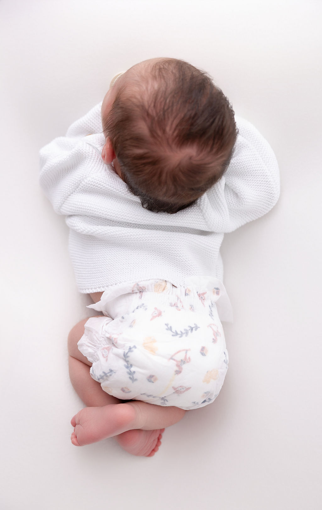 A look down at a newborn in a white sweater sleeping on its tummy thanks to parenting classes in torrance ca