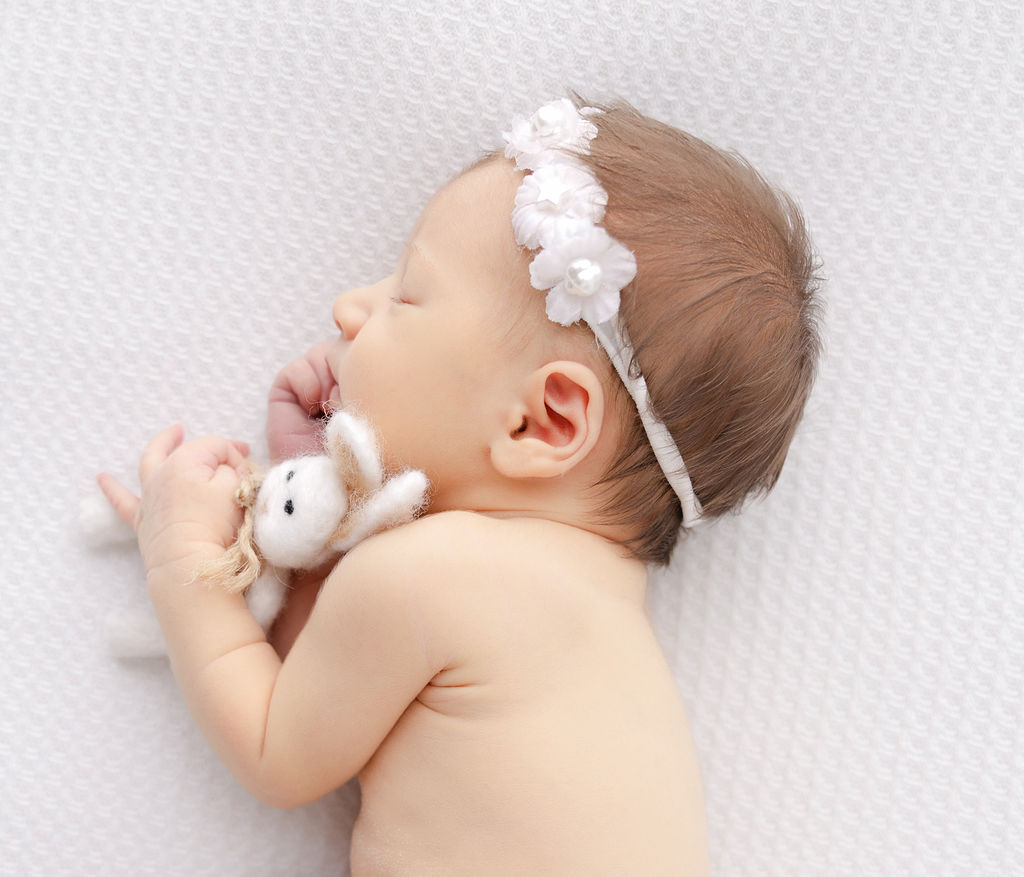 A newborn baby girl sleeps cuddling a felt bunny wearing a flower headband