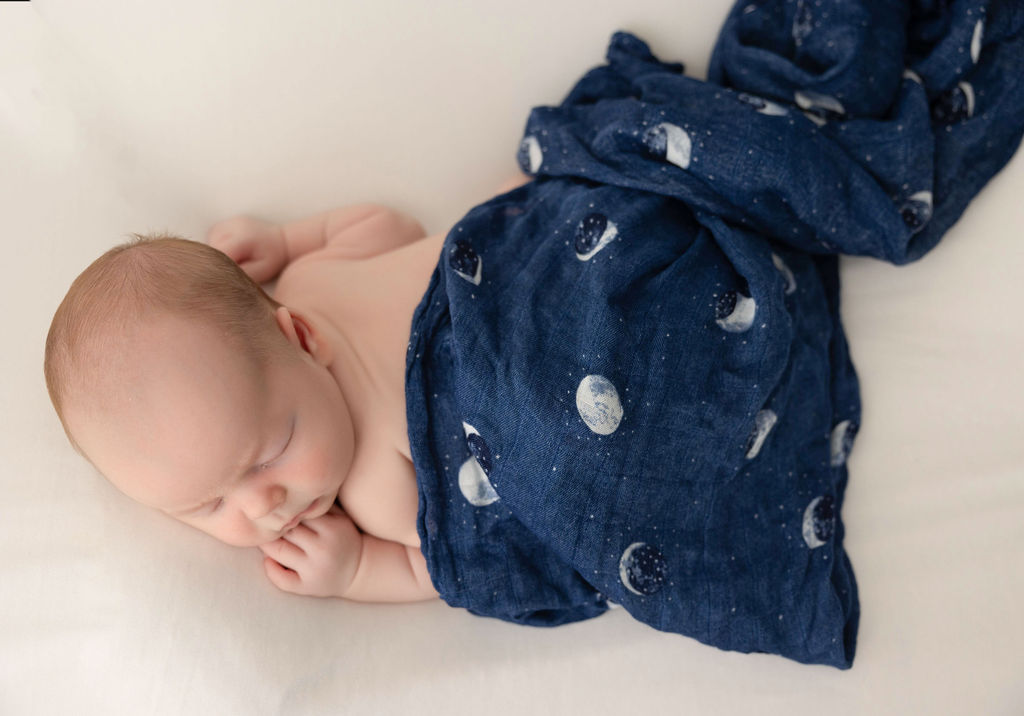 A newborn baby sleeps under a moon blanket in froggy pose after mom found some pelvic floor therapy in Torrance