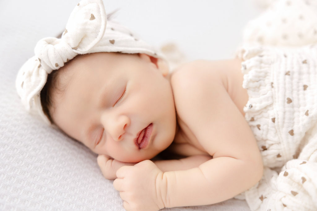 A baby girl sleeps with mouth open ina. heart covered bow and matching balnket