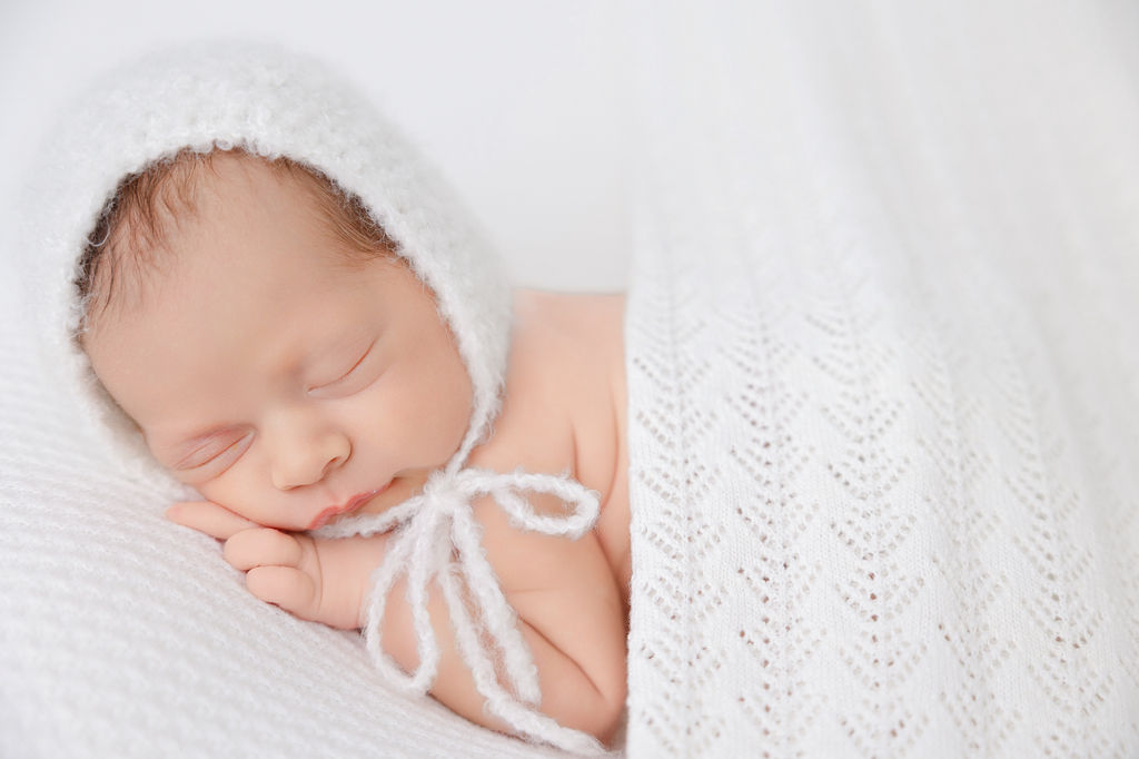 A sleeping newborn in a white bonnet on its tummy under a white blanket after mom enjoyed placenta encapsulation in torrance ca