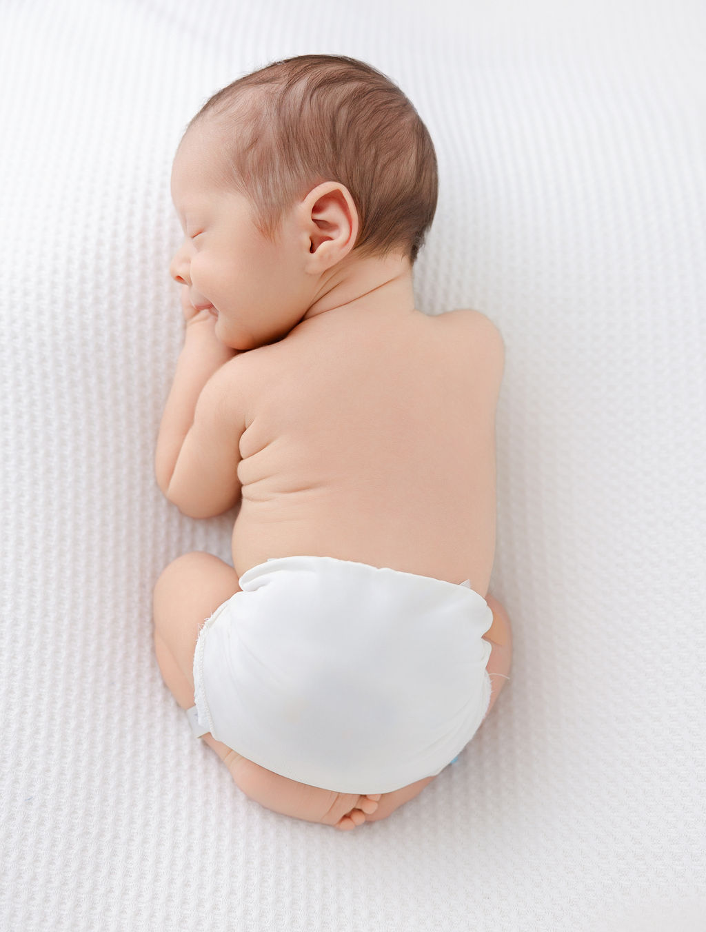 A newborn baby sleeps in froggy pose in a diaper on a whtie bed after mom found placenta encapsulation in torrance ca