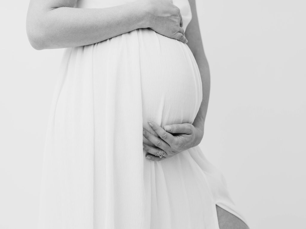 Details of a mother to be's hands on her bump in a white maternity dress after visiting prenatal chiropractors in torrance