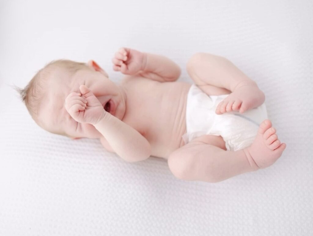 Newborn baby boy curled up in just a diaper and letting out a cry