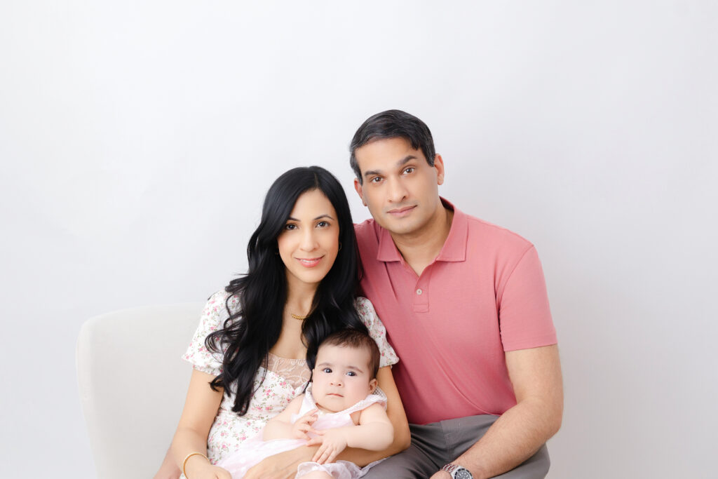 Father, mother, and 6 month old baby girl wearing different shades of pink and posed for a family portrait session at Heather Nicole Photography Studio