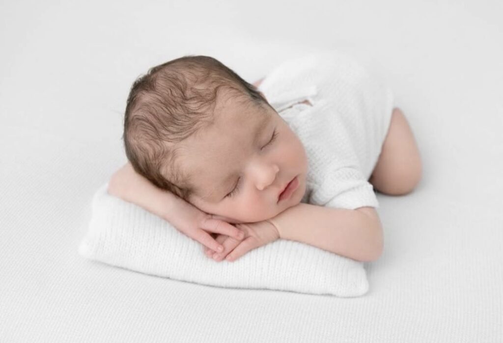 Newborn baby boy posed on belly with his hands folded for photoshoot 
