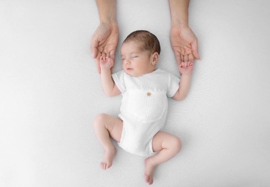Newborn Baby Girl Lying on Back While Her Hands Draped Softly in Dad's Hands